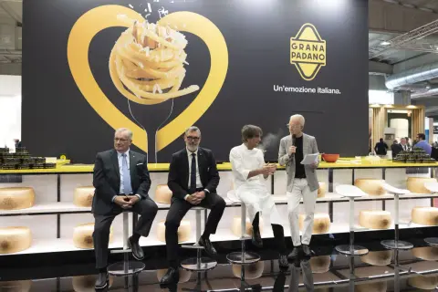 Män sitter på stolar framför en stor vägg med en bild av pasta och texten "GRANA PADANO. Un'emozione italiana.