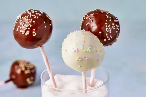 Leckere cake pops aus kuchenresten, verziert mit bunten Streuseln, stecken in einem Glas voller Zucker.