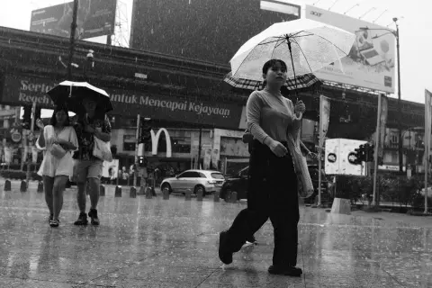 A woman with a clear umbrella walks in the rain, a tri x sign visible in the background.