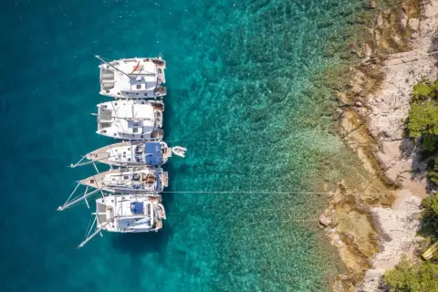 Flott bild av flera segelbåtar som ligger för ankar i turkost vatten nära en klippig kust. En dröm om att segla i Kroatien.