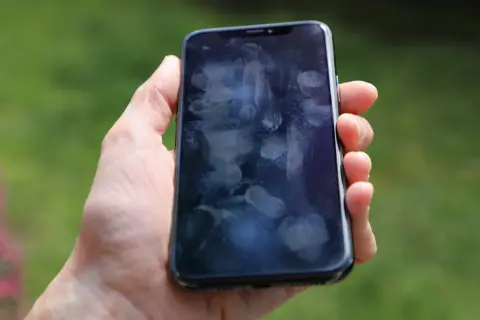 Dłoń trzyma smartfon z licznymi śladami palców na ekranie. Czy to efekt braku szkła hartowanego 9D?