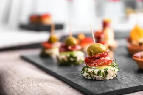 Wykwintne koreczki na imprezę: oliwka, salami i świeży koperek na chrupiącym pieczywie. Idealne na przyjęcie!