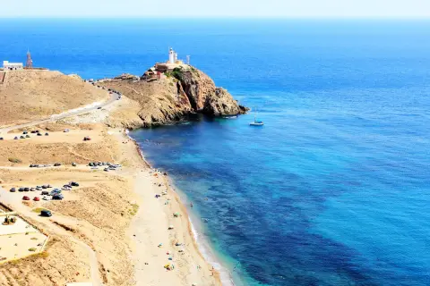 Un faro preside la costa, ideal para saber qué hacer en Cabo de Gata. Playas, mar azul y un velero invitan al relax.