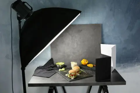 A food photography setup with burgers, salad, and a yellow pepper, illuminated by a large softbox, showcasing effective diy photography lighting.