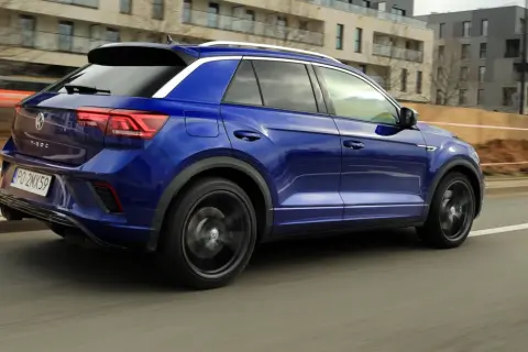 Niebieski Volkswagen T-Roc pędzi ulicą. W tle nowoczesne budynki i plac budowy.