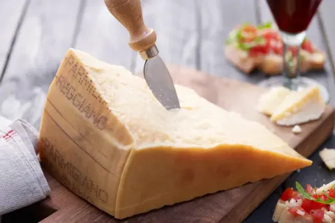 Ein großes Stück Parmesan mit einem Messer, daneben Bruschetta und ein Glas Rotwein.