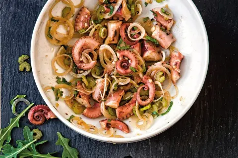 Un delicioso salpicón de pulpo con cebolla y perejil, servido en un plato blanco sobre una pizarra oscura.