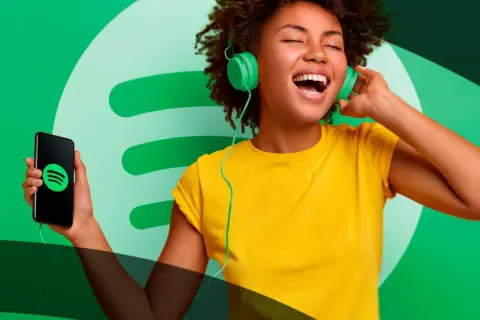 A woman with headphones sings along to music from her phone, showcasing the joy of Spotify social media.