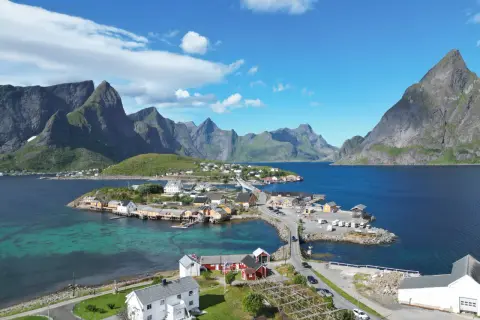 Idyllisches Dorf an der Küste mit roten und weißen Häusern, umgeben von majestätischen Bergen. Tolle Lofoten Tipps für Ihren Urlaub!