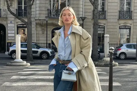 Elegancka kobieta w beżowym trenczu, błękitnej koszuli i jeansach, prezentująca stylowy sposób, jak nosić trencz. Paryskie uliczne klimaty.