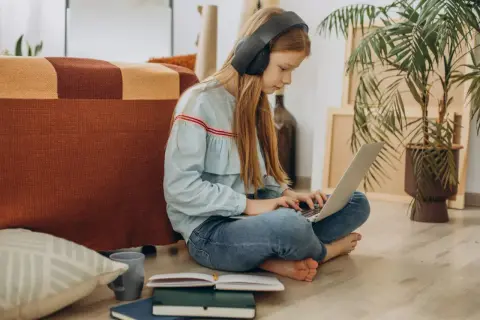 Dziewczynka w słuchawkach uczy się na laptopie, przygotowując argumenty, jak przekonać rodziców do szkoły w chmurze.