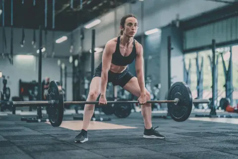 Femme concentrée en position pour un soulevé de terre, haltères lourds prêts à être soulevés dans une salle de sport.