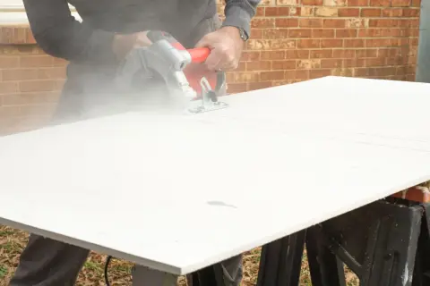 A person demonstrates how to cut cement board with a circular saw, creating a cloud of dust.