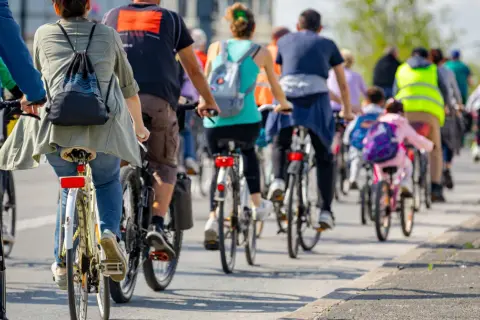 Grupa rowerzystów jedzie w kolumnie, przestrzegając przepisów. Widać plecaki i odblaskowe kamizelki.