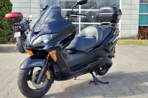 Czarny skuter Honda Forza 250 z kufrem na bagaż, zaparkowany przed budynkiem.