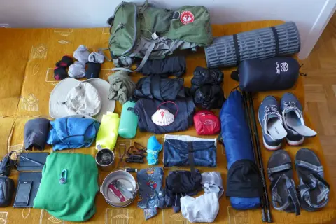 Przygotowania do camino de santiago: plecak, buty, śpiwór, karimata, ubrania, czapka, kijki i muszla pielgrzyma.