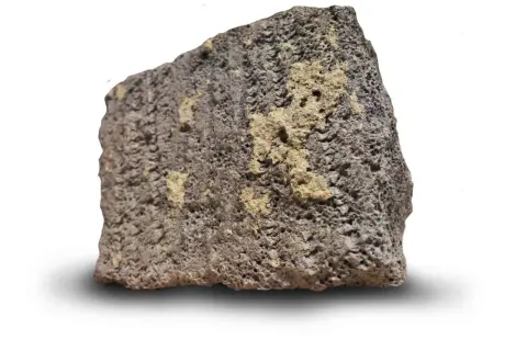 En bit porös, mörkgrå sten med ljusare gula partier. Så här ser blåbetong ut, en lätt och isolerande sten.