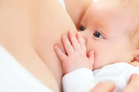 Ein Baby trinkt an der Brust. Die Hand des Babys ruht auf der Brust, was die Milchproduktion anregen kann.