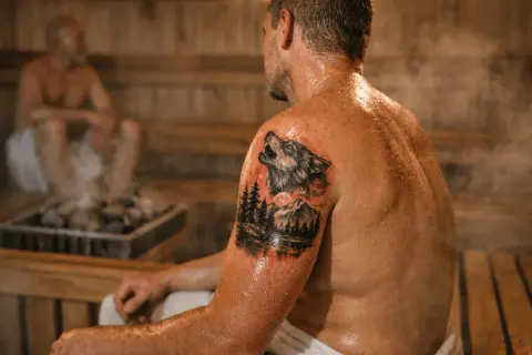Mann mit Wolf-Tattoo in der Sauna. Dampf steigt von den heißen Steinen auf.