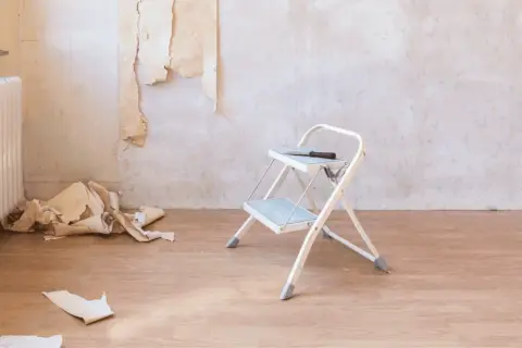 Tapete entfernen ist zeitaufwendig. Ein kleiner Tritt, Werkzeug und Tapetenreste liegen auf dem Holzboden.