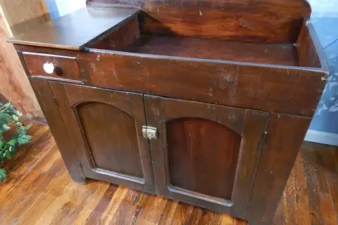 A vintage wooden dry sink with a drawer and cabinet doors, perfect for a rustic kitchen or bathroom.