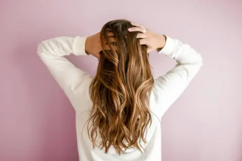 Mujer con pelos largos y ondulados, de color castaño, jugando con su cabello.