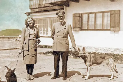 Eva Braun, hitlers fru, står med en hund. Bredvid henne står en man i uniform med en annan hund.