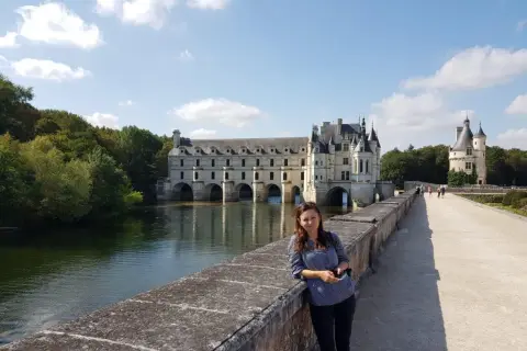 Kobieta na tle zamku Chenonceau nad rzeką w słoneczny dzień.