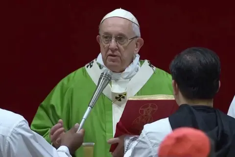 Papst Franziskus in grüner Messrobe hält eine Anrede. Vor ihm ein rotes Buch mit einem Bild.