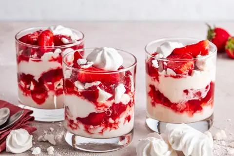 Drei Gläser mit Eton Mess: geschichtete Erdbeeren, Sahne und zerbrochene Baiser-Stücke. Ein süßer Genuss!