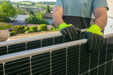 Un técnico de placas solares instala paneles en un tejado con vistas a un pueblo.