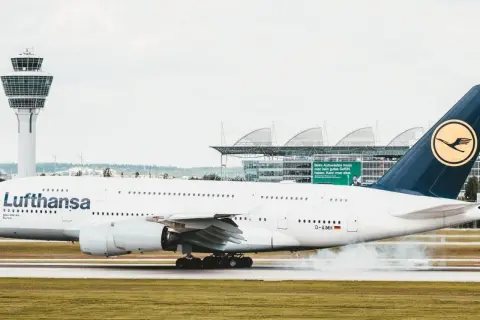 Lufthansa-Flugzeug landet auf dem Rollfeld, Rauch steigt auf.
