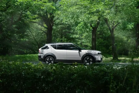 Biały Tucson Hybrid na tle zielonego lasu. Niskie spalanie to jego atut podczas podróży po malowniczych trasach.