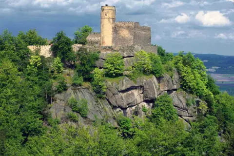 Zamek Chojnik góruje nad skalistym zboczem, otoczony bujną zielenią drzew.
