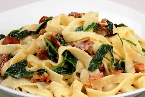 Pyszny makaron tagliatelle z kremowym sosem mascarpone, szpinakiem i chrupiącym boczkiem.