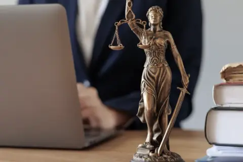 Justitia-Statue neben Laptop und Büchern. Ein Anwalt prüft Unterlagen, vielleicht wegen eines Widerspruchs Pflegegrad.