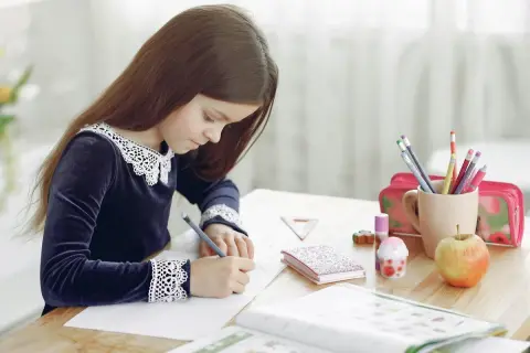 Niña concentrada en su dictado 2 primaria, rodeada de útiles escolares, un libro abierto y una manzana.