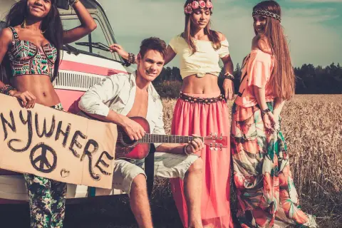 Neo-Hippies mit Gitarre und Schild "Anywhere" vor einem Van in einem Feld.