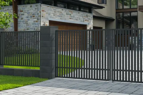 Nowoczesne ogrodzenie z ciemnoszarego metalu, z solidnymi słupkami, idealnie pasuje do domu z kamienną elewacją. Taka wysokość ogrodzenia bez pozwolenia zapewnia prywatność.