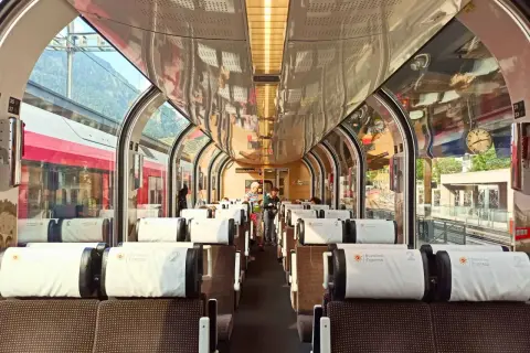 Wnętrze pociągu panoramicznego Bernina Express z wygodnymi siedzeniami i dużymi oknami, przez które widać góry.