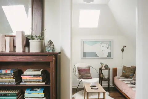 Accogliente libreria in mansarda con un letto, una poltrona e un quadro.
