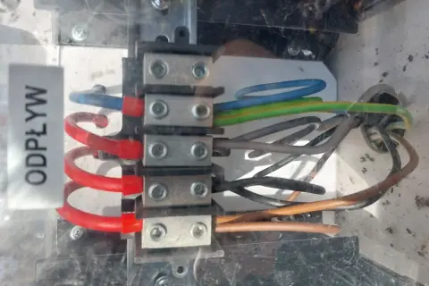 Widok z bliska na zaciski elektryczne z podłączonymi przewodami w różnych kolorach (niebieski, zielono-żółty, brązowy, czarny).