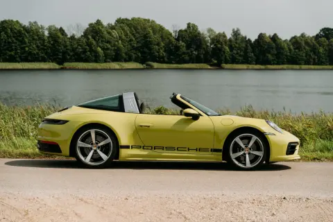 Żółty Porsche Targa z czarnym napisem na progu, zaparkowany nad jeziorem, otoczony zielenią.