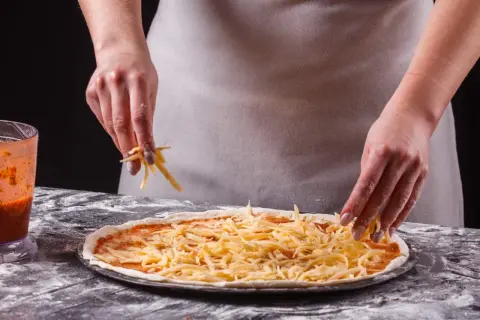 Ręce posypują pizzę startym serem. Zastanawiasz się, jaki ser do pizzy będzie najlepszy? Ten wygląda apetycznie!