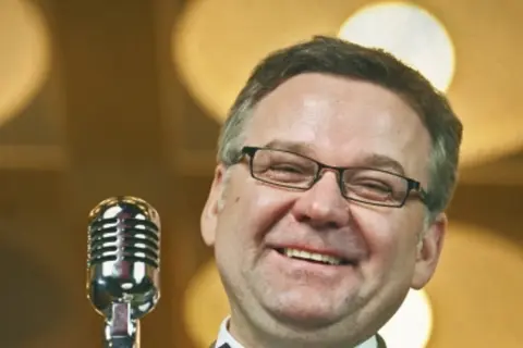 Artur nagrał płytę myśliwiecka. Uśmiechnięty mężczyzna w okularach stoi przy mikrofonie.