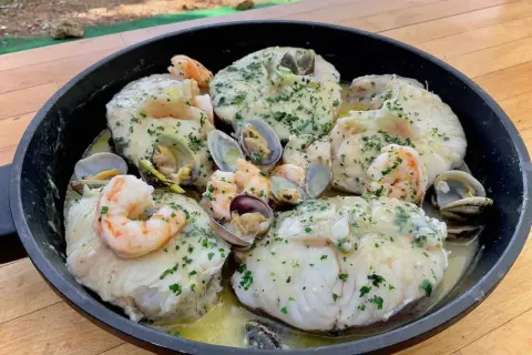 Merluza con almejas y gambas en una sartén, con perejil picado y salsa cremosa. ¡Un plato marinero delicioso!