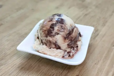 Ein Löffel cremiges Kinderriegel Eis mit Schokoladenstückchen auf einer weißen Schale.