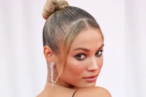 Elegancka, gładka fryzura typu sleek bun z błyszczącymi kolczykami.