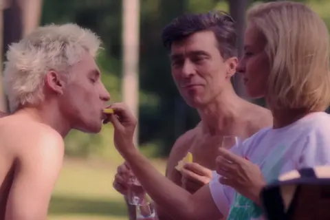 Trzy miłości film: blondyn z cytryną, mężczyzna wpatrzony w kobietę, która karmi blondyna.