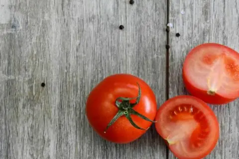 Tomates frescos, uno entero y dos cortados por la mitad, sobre una tabla de madera. Son un ejemplo de 10 alimentos umami.